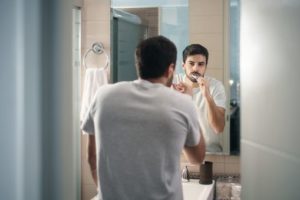 Man looking in mirror brushing his teeth. | Maurstaf family denstistry.